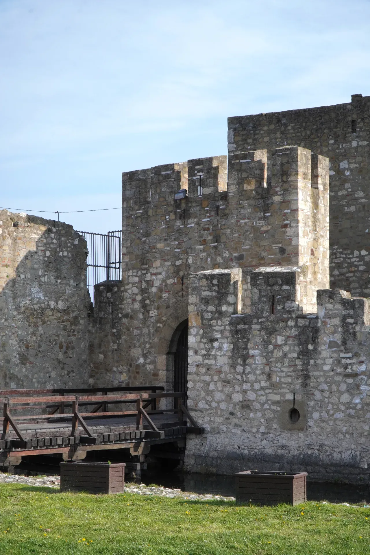 Un ponte levatoio in legno conduce a un cancello in pietra della Fortezza di Smederevo in Serbia, fiancheggiato da un fossato e prati.