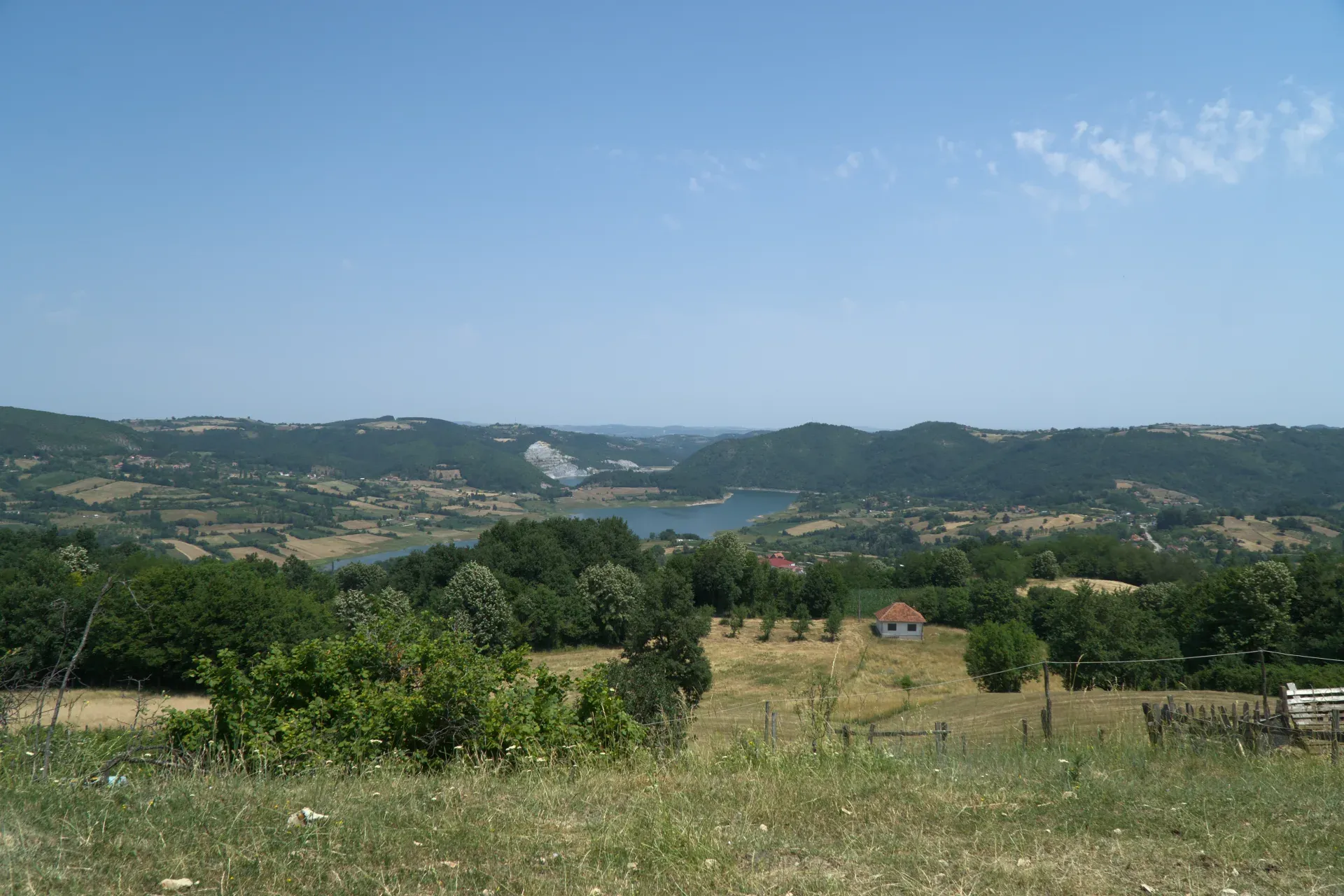 Paesaggio collinare con un lago e alberi verdi, sulla strada per il Parco Nazionale di Tara in Serbia, con una piccola casa in lontananza.
