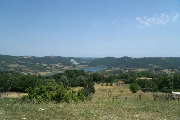 Hilly landscape with a lake and green trees, on the way to Tara National Park in Serbia, with a small house in the distance.