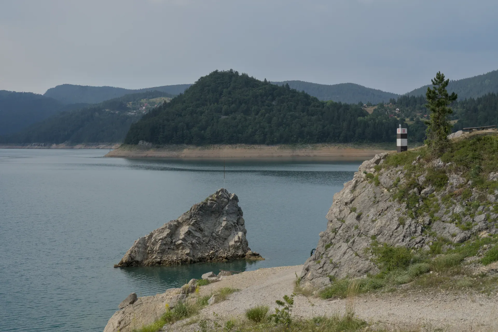 Zaovine See im Nationalpark Tara, Serbien, mit grünen Bergen, Felsen und einem Leuchtturm.