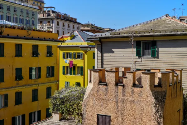 Fassaden von gelben Gebäuden mit grünen Fensterläden und steinerner Struktur in Genua bei strahlendem Sonnenschein.