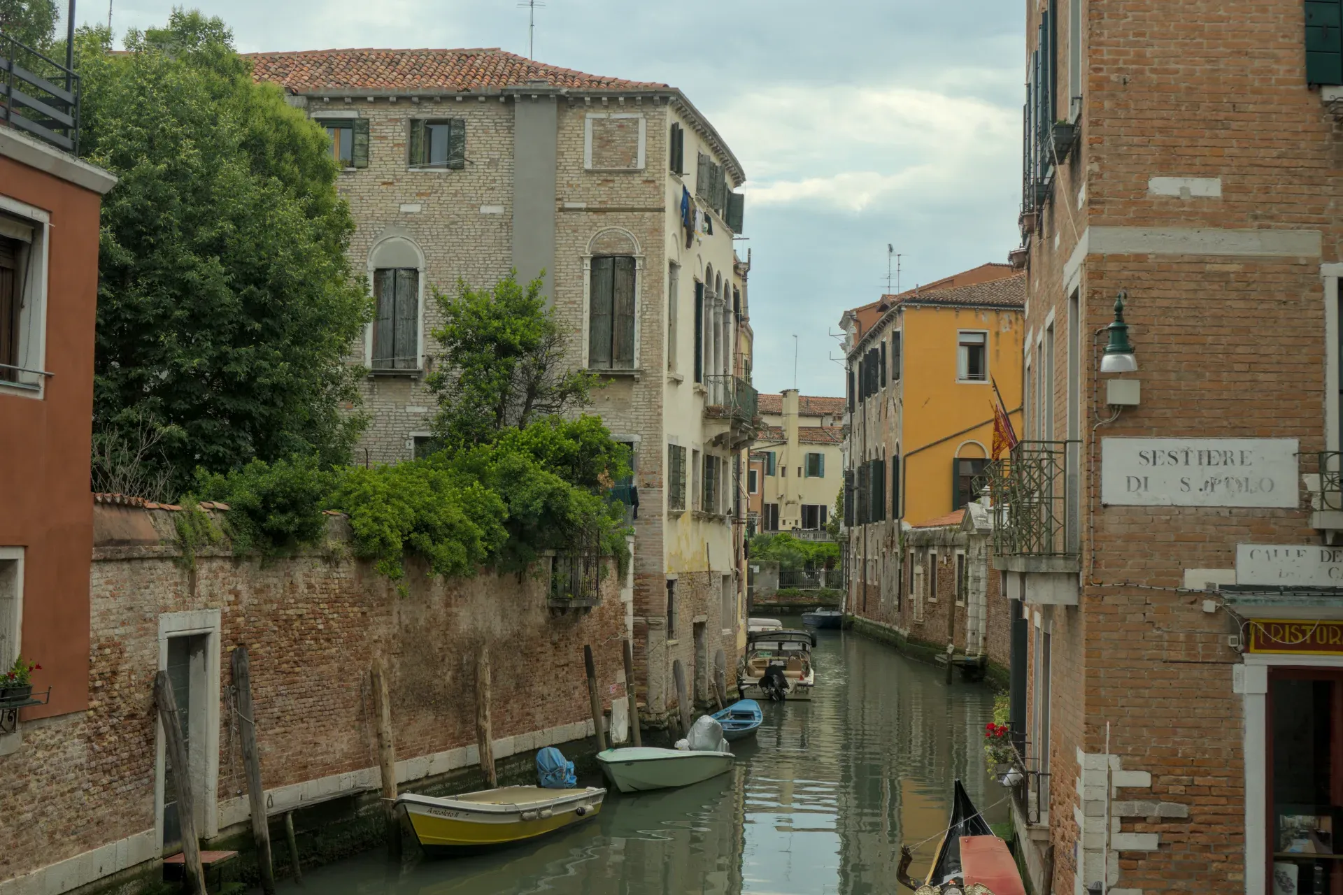 Uno stretto canale veneziano con edifici tradizionali, vegetazione verde e diverse barche che galleggiano nell'acqua.