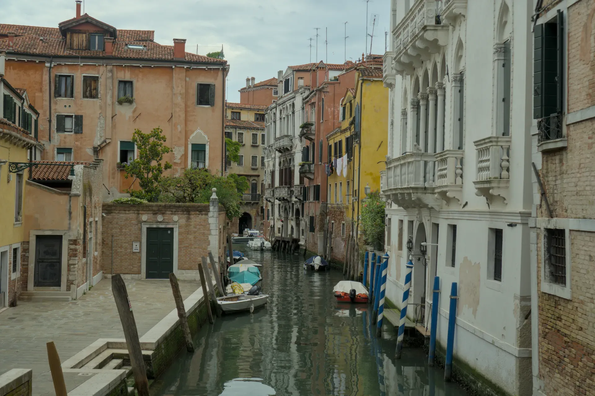 Ein schmaler Kanal in Venedig, gesäumt von historischen Gebäuden und mit mehreren Booten, die im Wasser liegen.