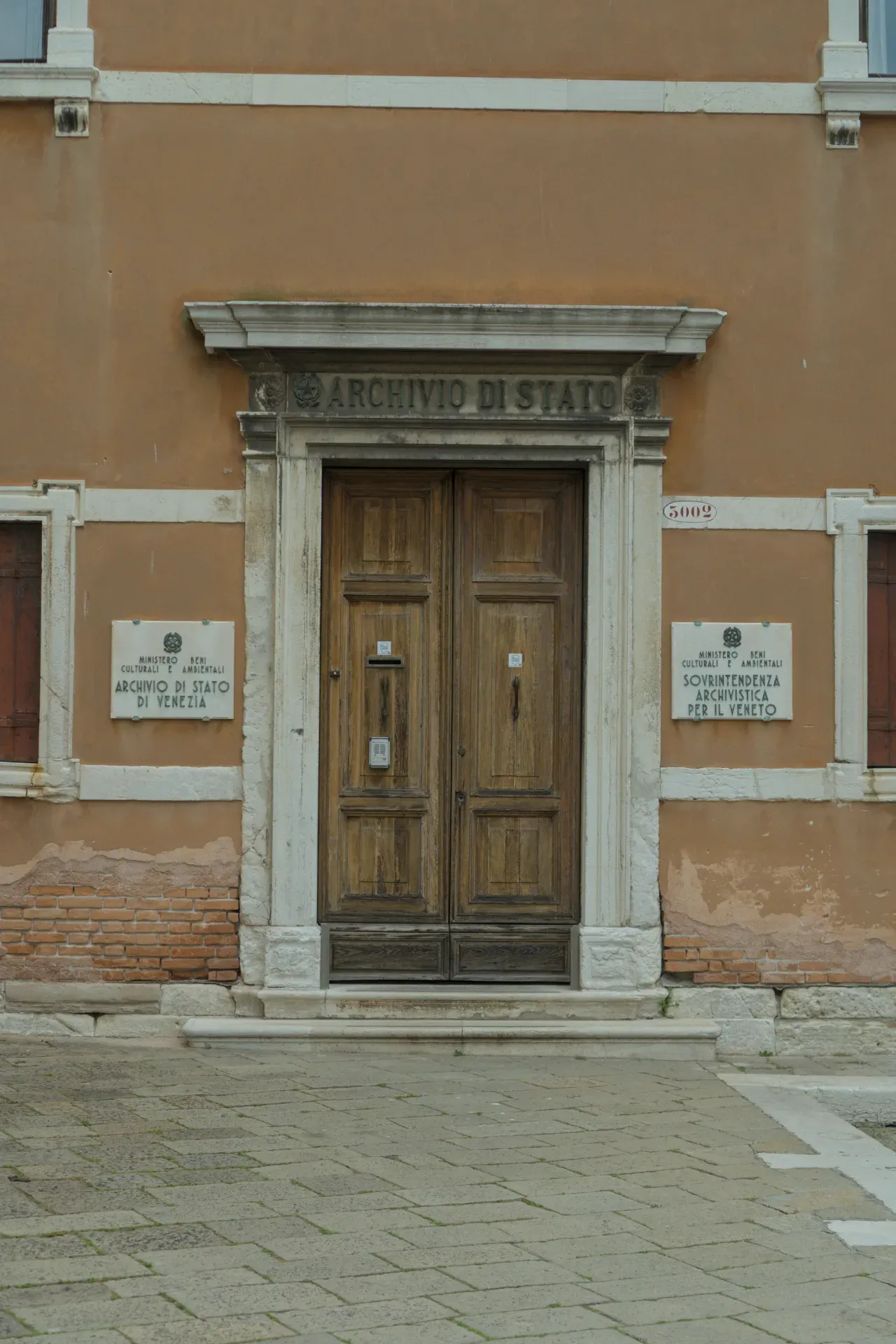 Un'ampia porta antica in legno all'ingresso dell'Archivio di Stato a Venezia, incorniciata da colonne di pietra e una facciata ocra.