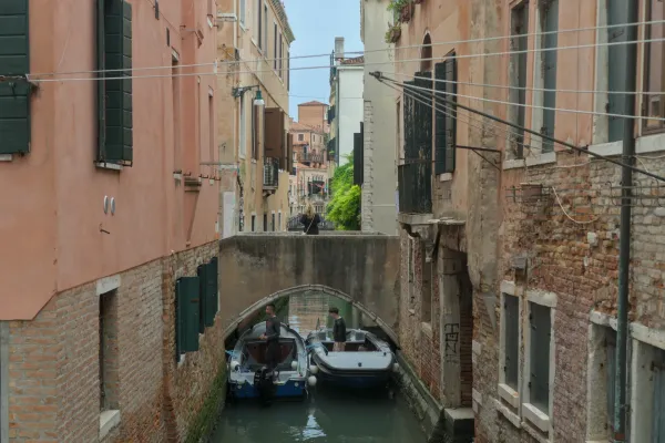 Venezianischer Kanal mit zwei Booten und Personen unter einer Brücke, umgeben von alten Ziegelgebäuden.
