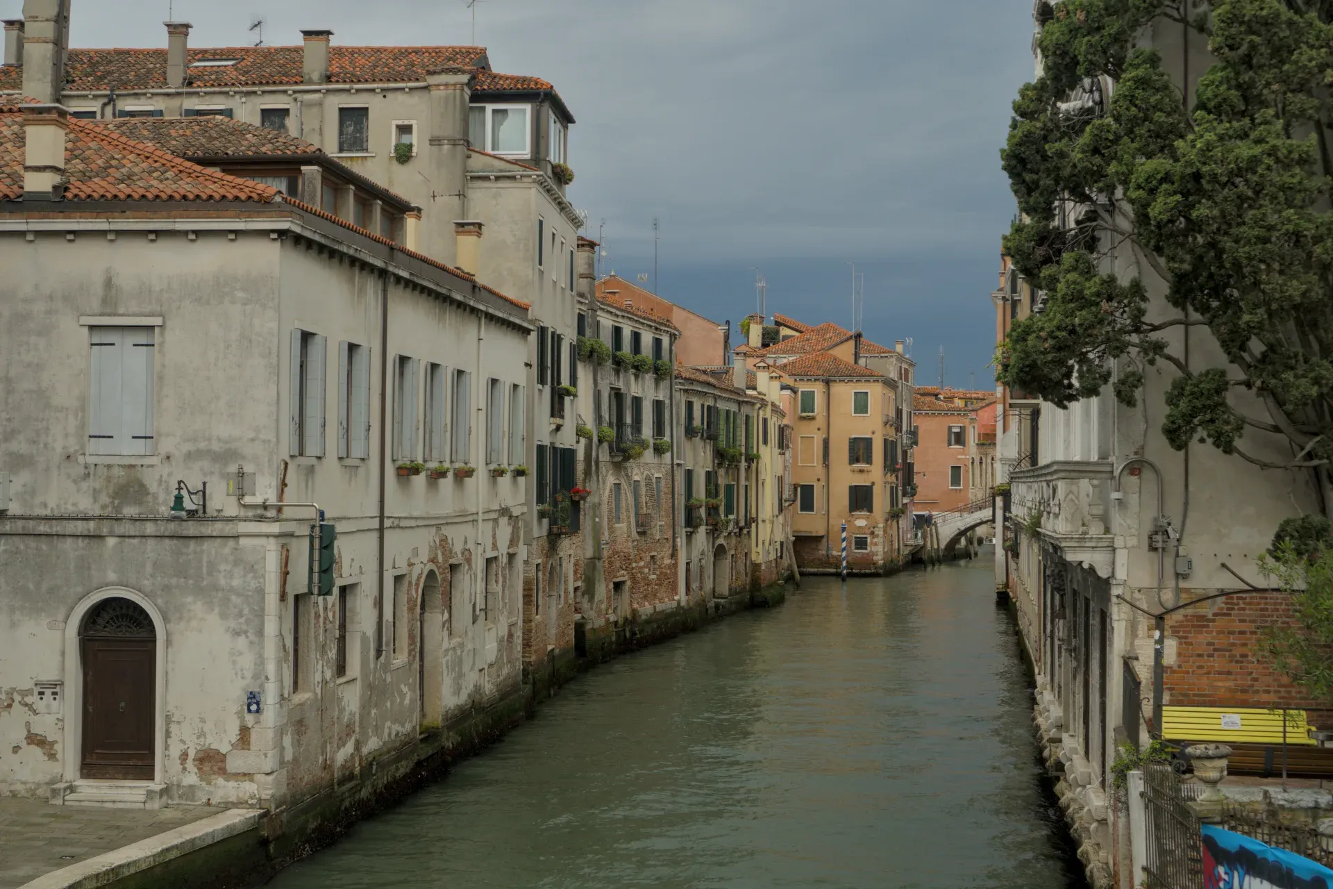 Uski kanal u Veneciji sa istorijskim zgradama i dramatičnim, oblačnim nebom.