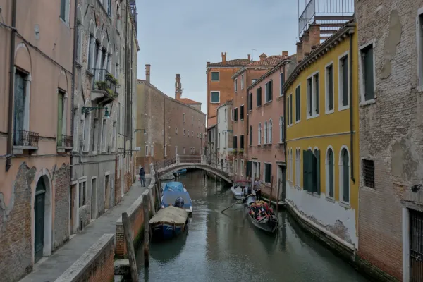 Un canale stretto a Venezia con una gondola, costeggiato da edifici storici colorati e un marciapiede.