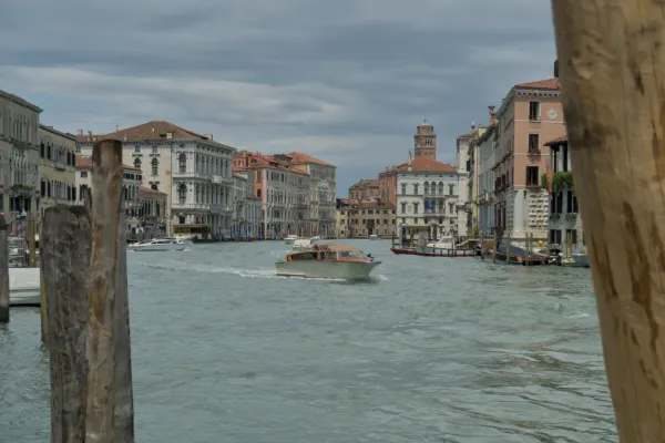 Una barca naviga sul Canal Grande a Venezia, circondata da edifici storici sotto un cielo nuvoloso.
