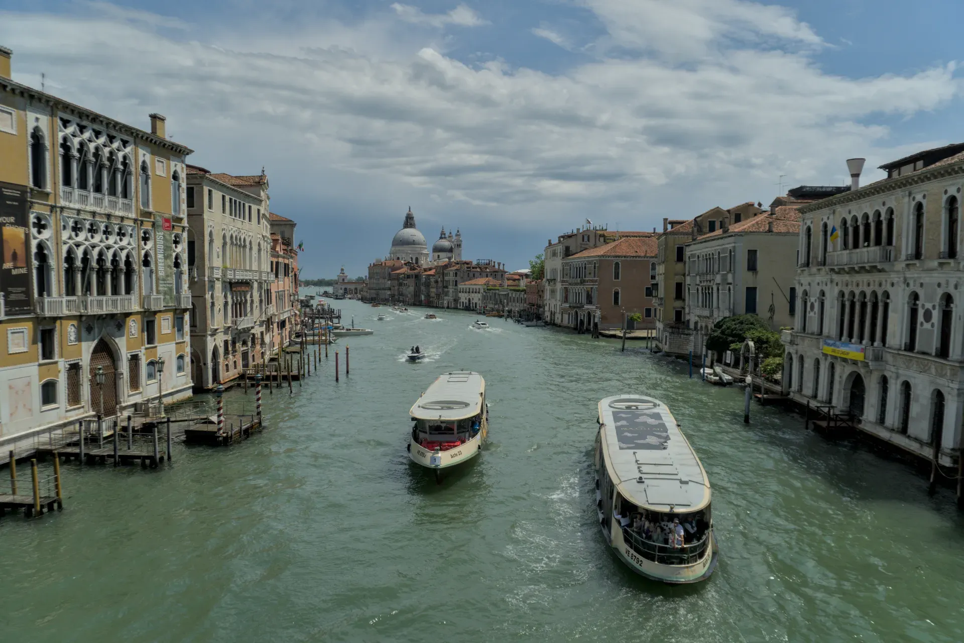Dos barcos navegan por el Gran Canal en Venecia, flanqueados por palacios históricos y una cúpula en el fondo.