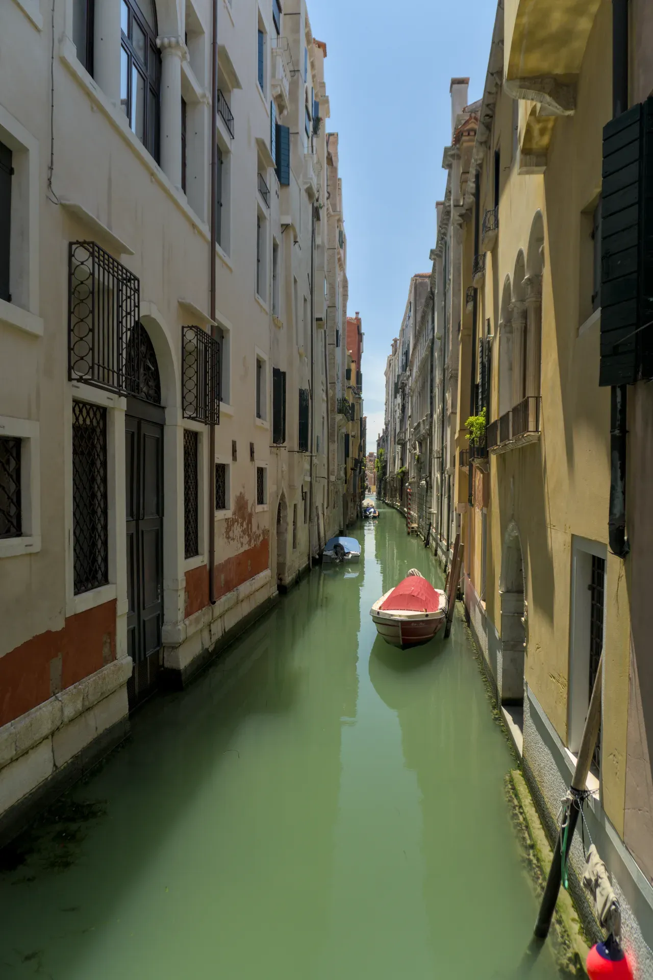 Enge venezianische Gasse mit einem Boot im smaragdgrünen Wasser, umgeben von historischen Gebäuden.