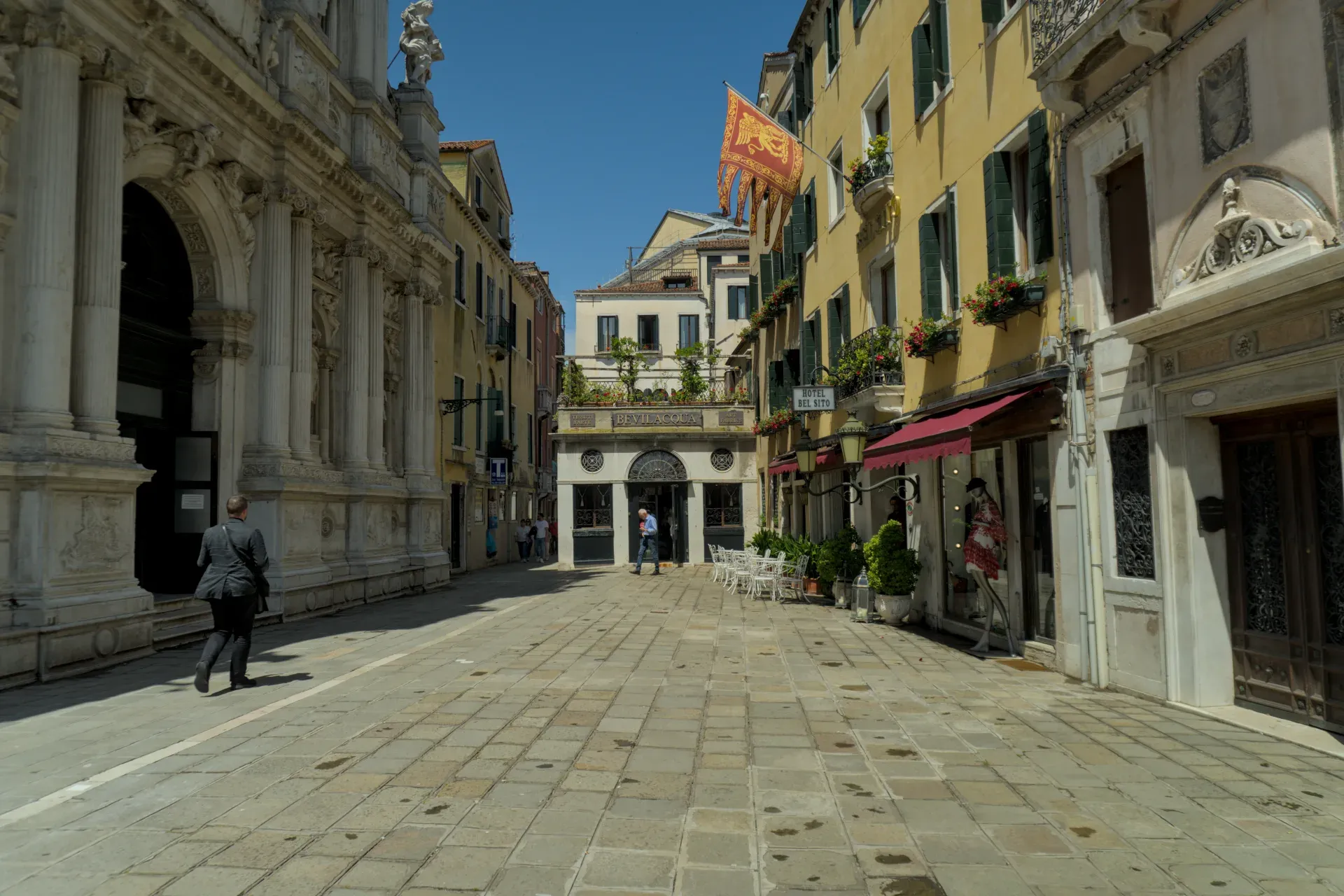 Une ruelle pavée à Venise avec des bâtiments historiques, un homme en costume et une bannière rouge.