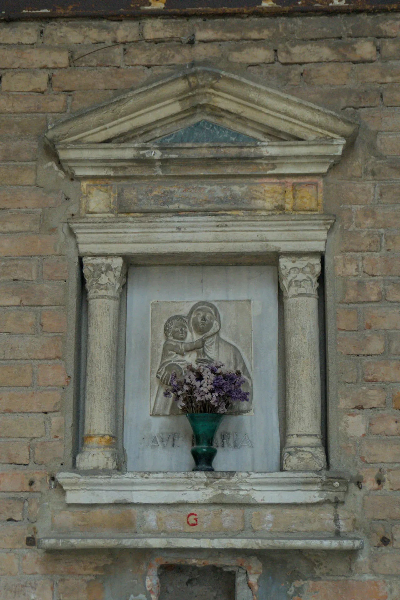Scultura religiosa della Madonna col Bambino con fiori in una nicchia di pietra, adatta per la decorazione murale.