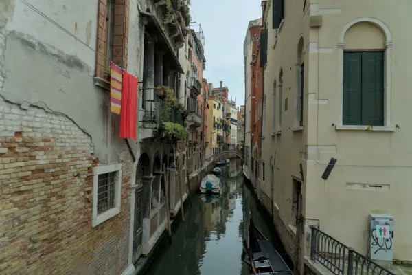 Ein schmaler venezianischer Kanal mit bunten Gebäuden, Wäsche, die von Balkonen hängt, und Booten im Wasser.