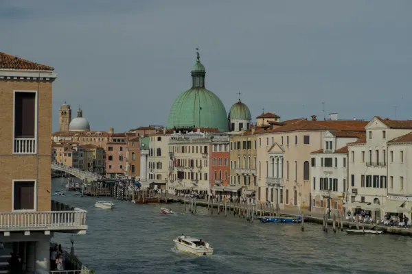 Foto paesaggistica del Canal Grande a Venezia, Italia, con edifici tradizionali e una prominente cupola verde sullo sfondo.