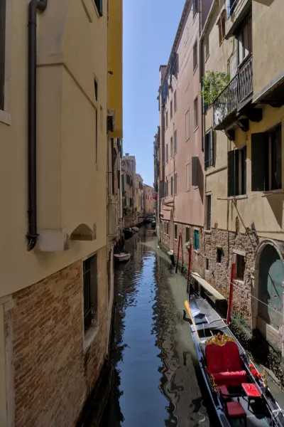 Venecijanski kanal sa gondolom, okružen istorijskim zgradama, u portretnoj orijentaciji.