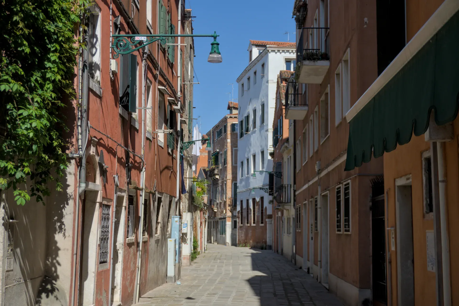 Sunčana, kaldrmisana ulica u Veneciji, pored tradicionalnih italijanskih kuća sa fasadama toplih boja.