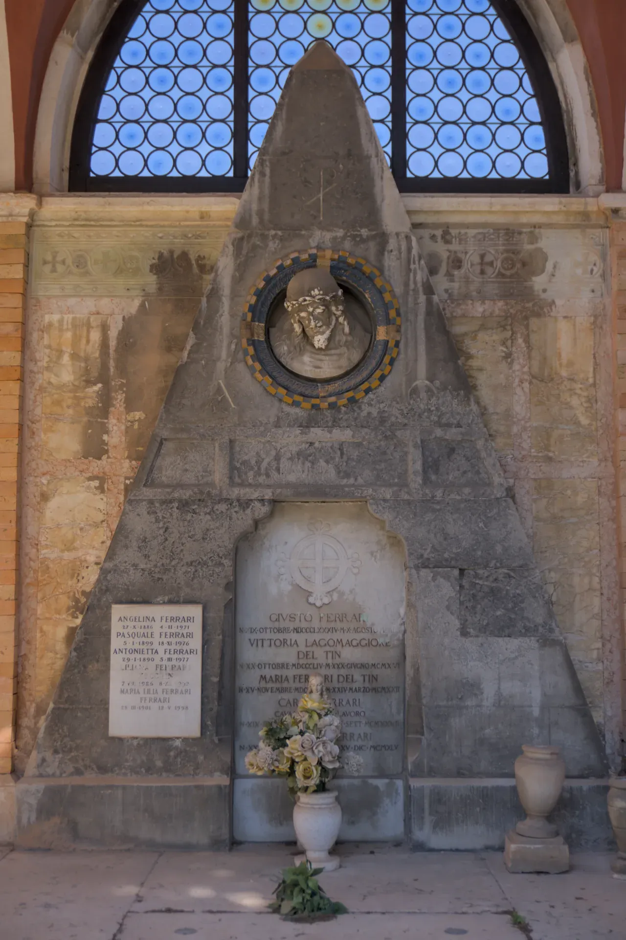 Ein ätherisches Porträt eines Grabmals auf dem Friedhof San Michele in Venedig, mit einer Büste und einem Blumenarrangement.