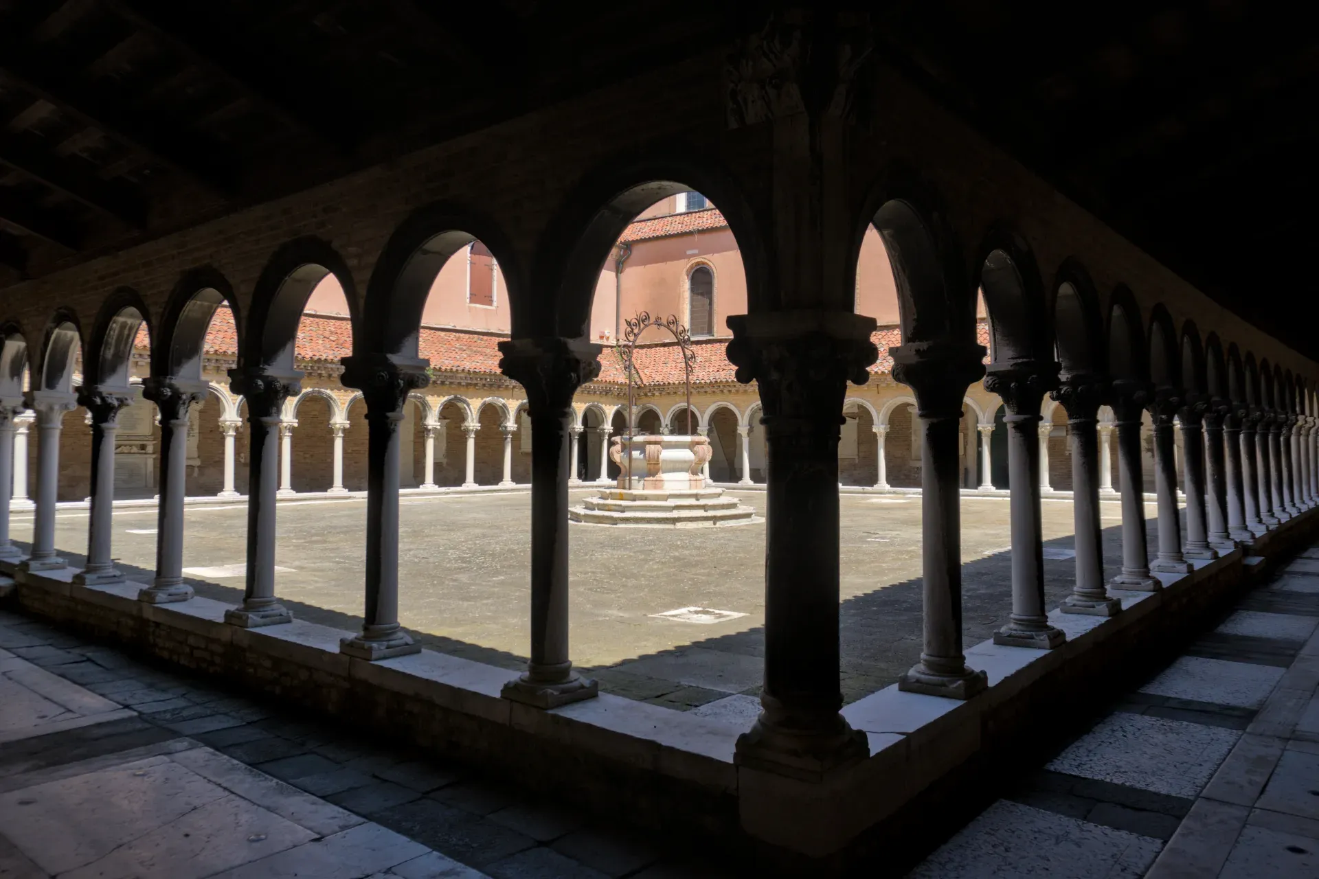 Patio arquitectónico en el Cementerio San Michele de Venecia con arcos, columnas y un pozo.