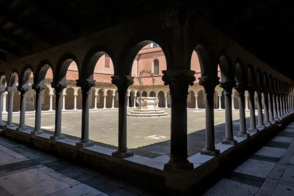 Cortile architettonico al Cimitero San Michele di Venezia con archi, colonne e un pozzo.