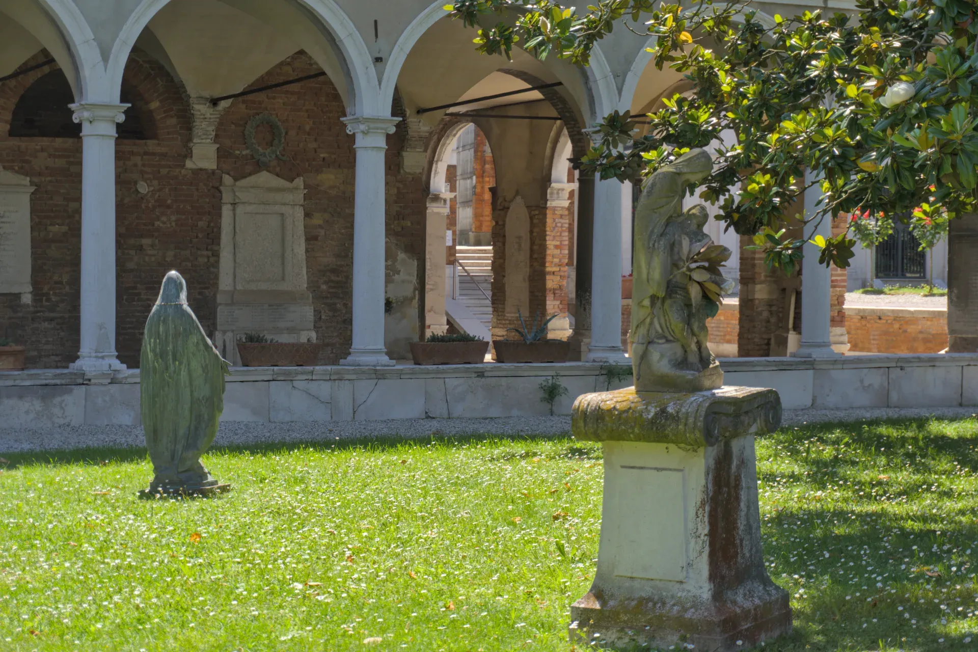 Friedhof San Michele Venedig mit Skulpturen und Arkaden im Sonnenlicht.
