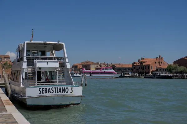 Boote im azurblauen Wasser der Lagune vor den Häusern von Murano, Venedig.