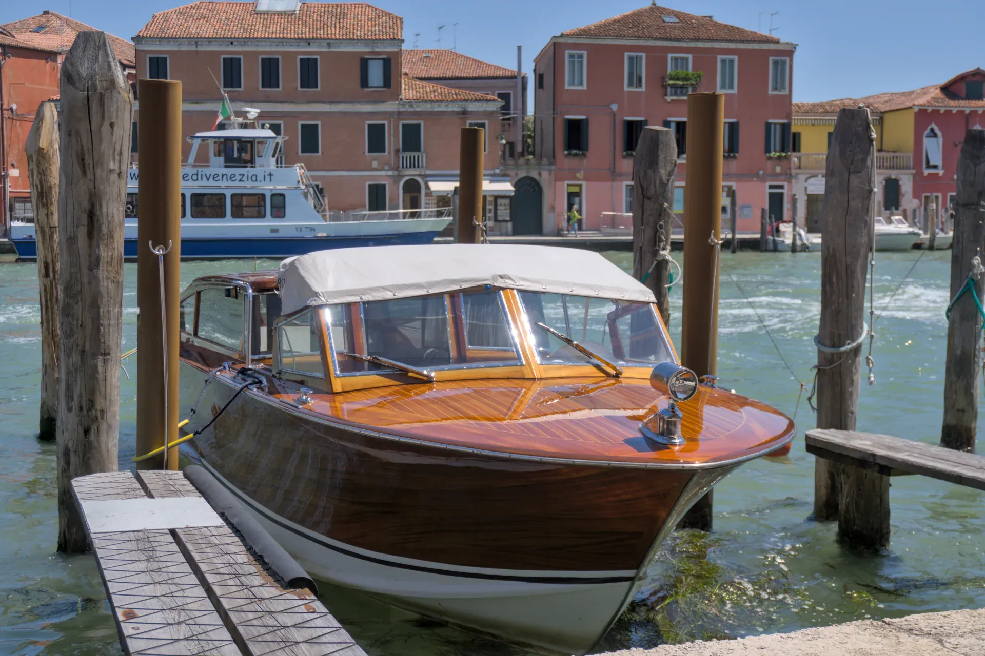 Lancha de madera anclada en el muelle de la isla de Murano en Venecia, con edificios tradicionales al fondo.