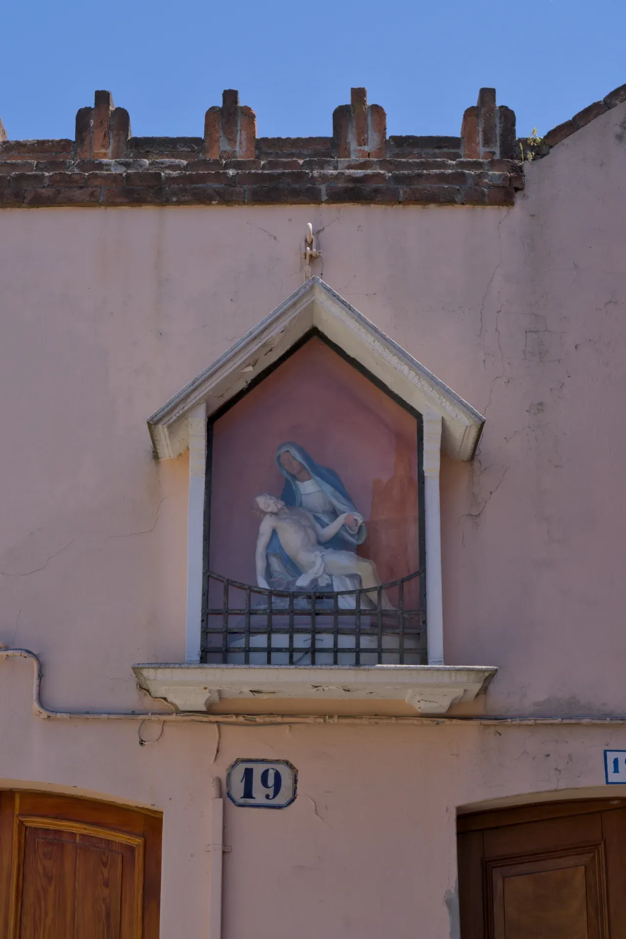 Fotografia d'arte di una rappresentazione della Pietà sull'isola di Murano, Italia, con un edificio intonacato di rosa e cielo blu.