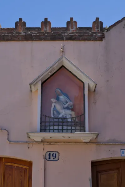 Fotografia d'arte di una rappresentazione della Pietà sull'isola di Murano, Italia, con un edificio intonacato di rosa e cielo blu.