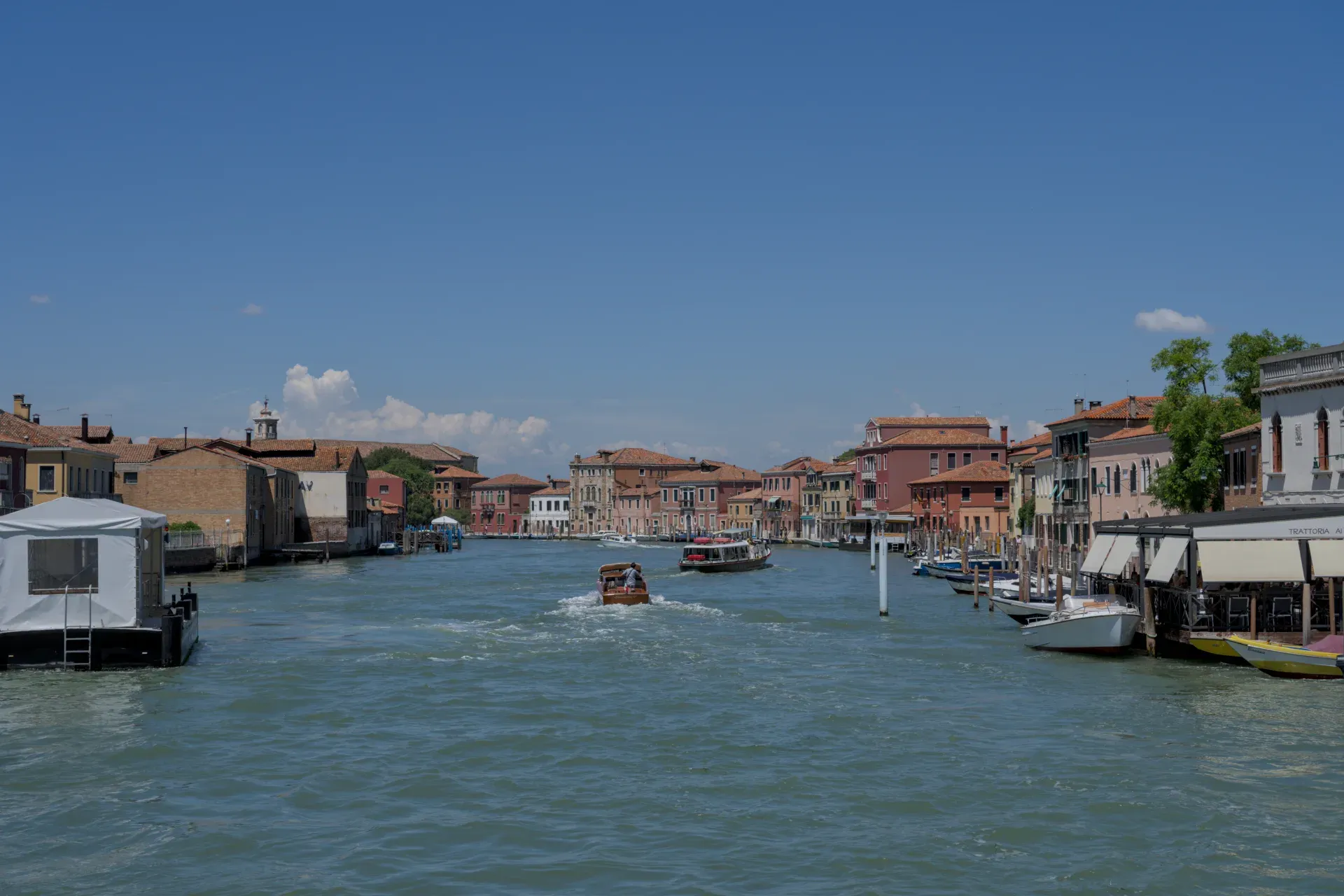 Blick auf einen Kanal auf Murano, Italien, mit bunten Gebäuden und Booten auf dem Wasser.