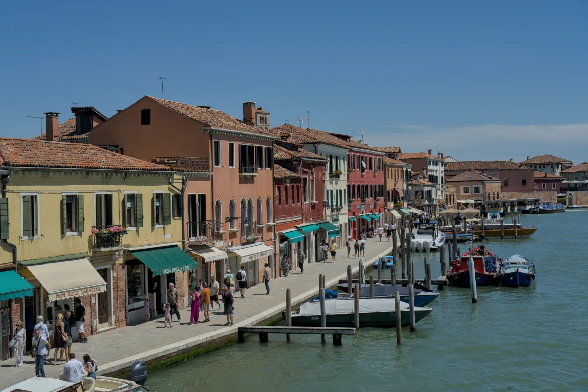 Case colorate lungo il canale sull'isola di Murano, Venezia, con barche e persone, in una giornata di sole.