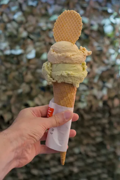 Ruka drži dupli sladoled od pistaća u kornetu od vafla sa vrhom od vafla, snimljen na Muranu.