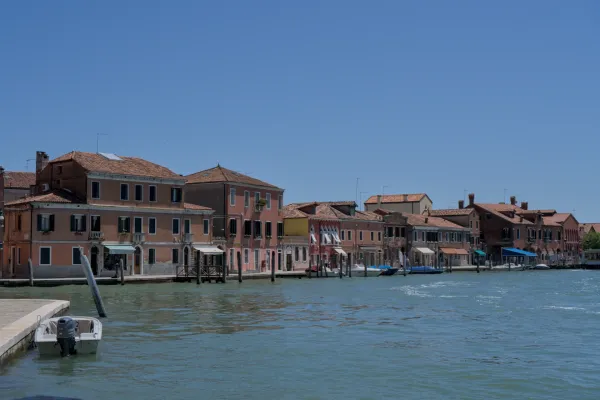 Niz zgrada sa terakotnim krovovima pored vode na ostrvu Murano, Italija, sa mirnom plavom vodom.