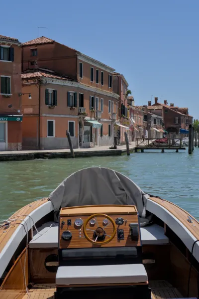 Blick vom Boot aus auf die Kanäle von Murano, Venedig, mit traditionellen Gebäuden und klarem Himmel.