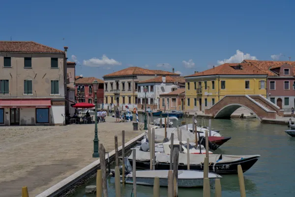 Die Insel Murano in Venedig zeigt einen Kanal mit Booten und einer traditionellen Steinbrücke, umgeben von farbenfrohen Häusern.