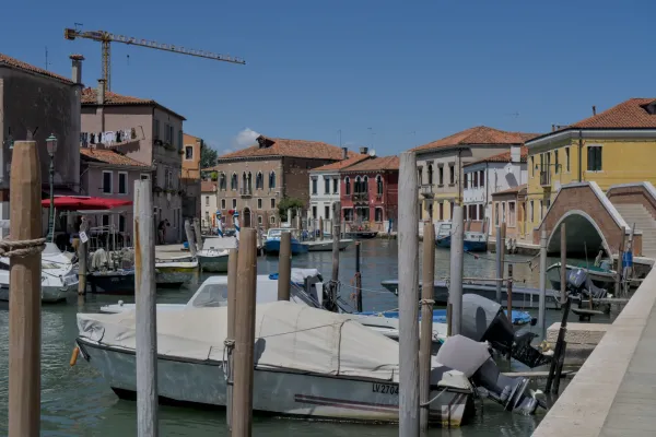 Boote im Kanal auf der Insel Murano, Venedig, mit bunten Häusern und blauem Himmel.