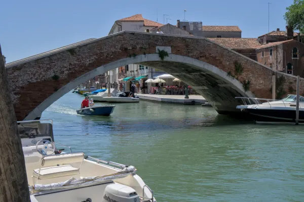 Historische Backsteinbrücke auf der Insel Murano, Venedig, überspannt einen Kanal mit kleinen Booten und Cafés.
