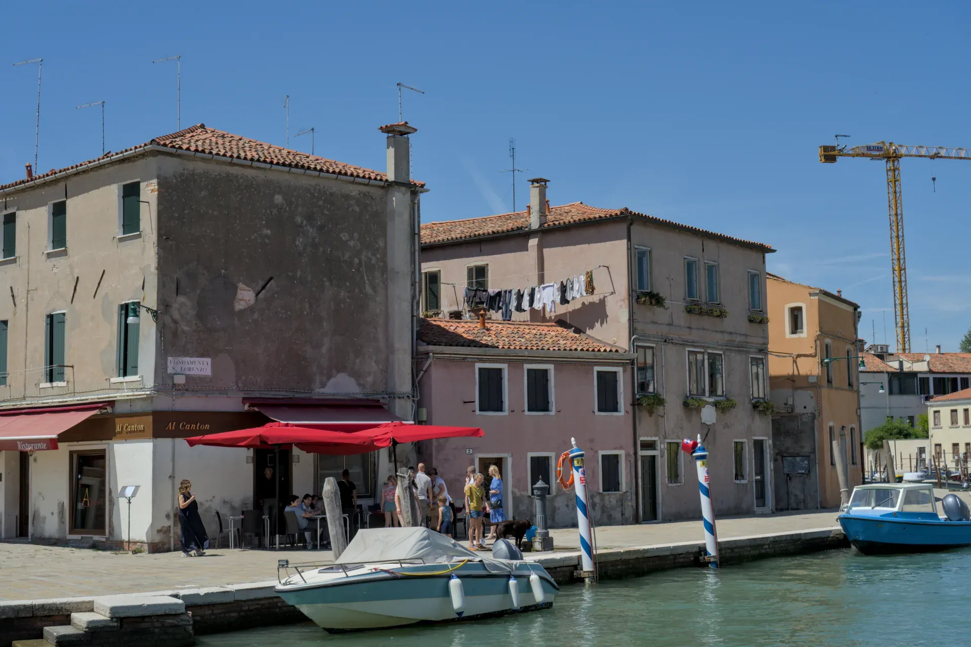 Fotografie des Kanalufers auf der Insel Murano mit Häusern, Wäsche und Booten im Wasser.