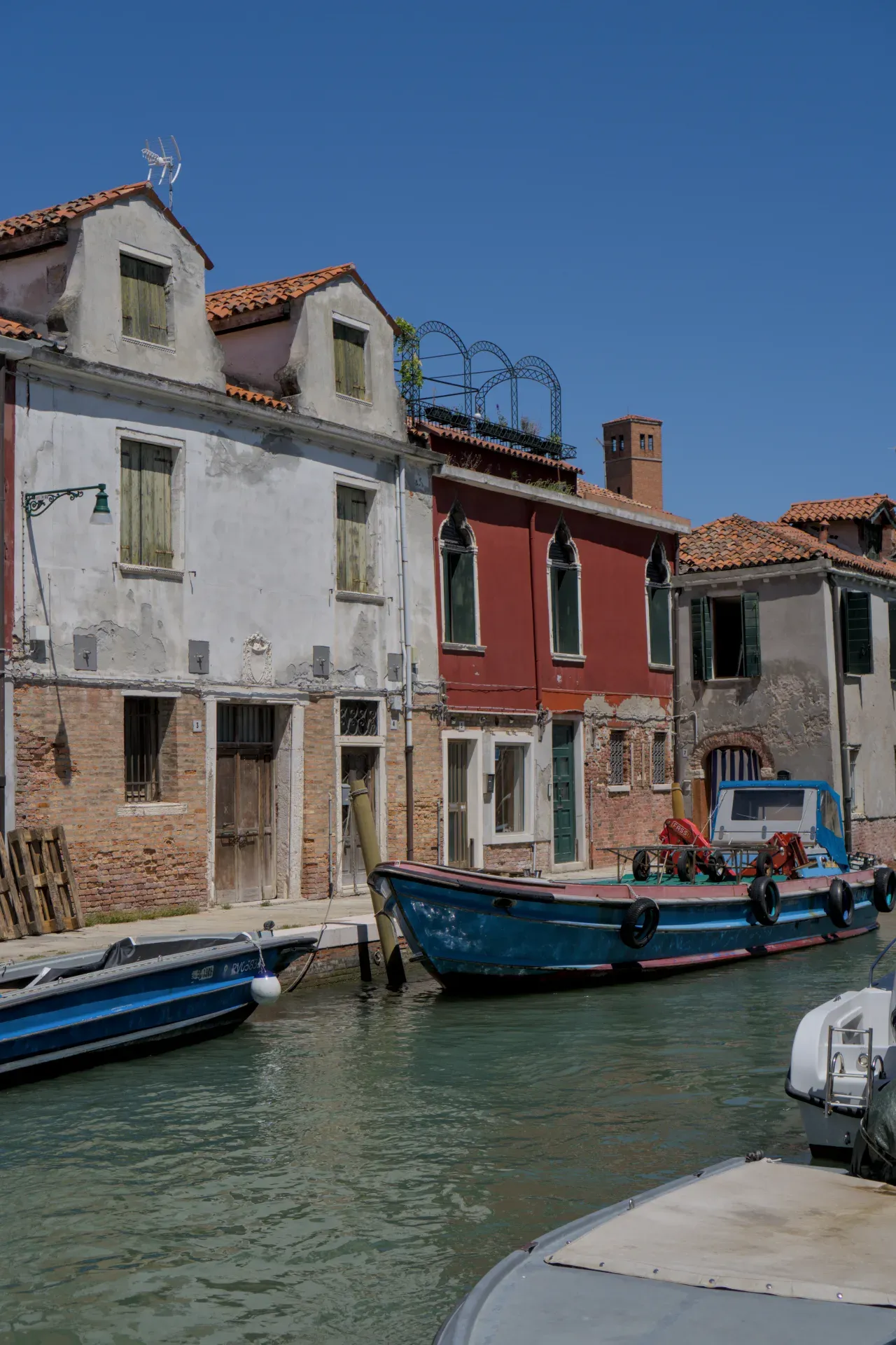 Eine ruhige Gasse auf der Insel Murano in Venedig mit traditionellen Gebäuden und Booten im Wasser.