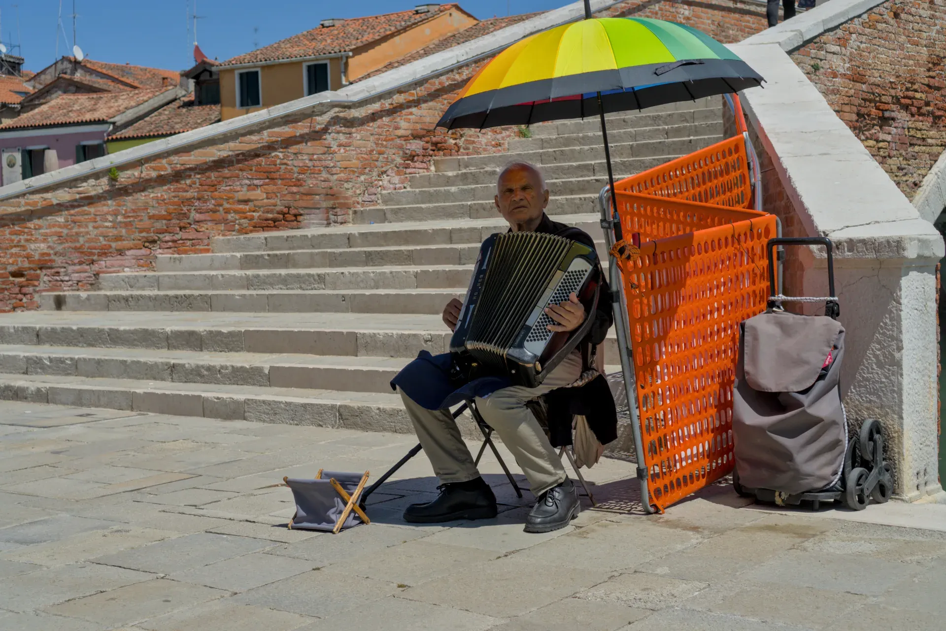 An elderly man plays the accordion on the island of Murano, Venice, Italy, under a colorful umbrella.