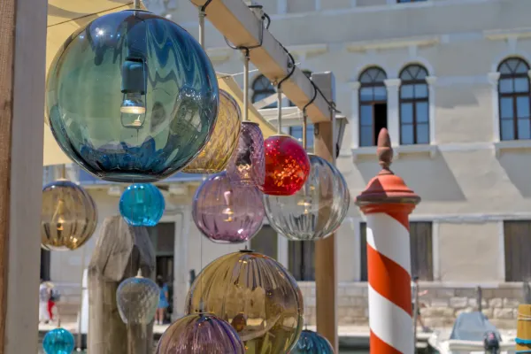 Šarene Murano staklene lampe koje vise iznad kanala u Italiji, sa fasadom zgrade u pozadini, inspirisane kafićem.