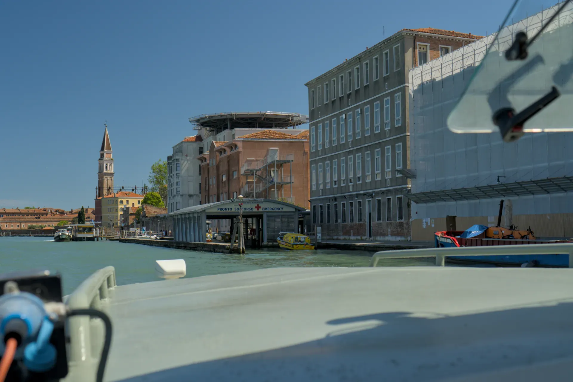 Vista del canale di Venezia con pronto soccorso, eliporto e campanile su sfondo di cielo azzurro.