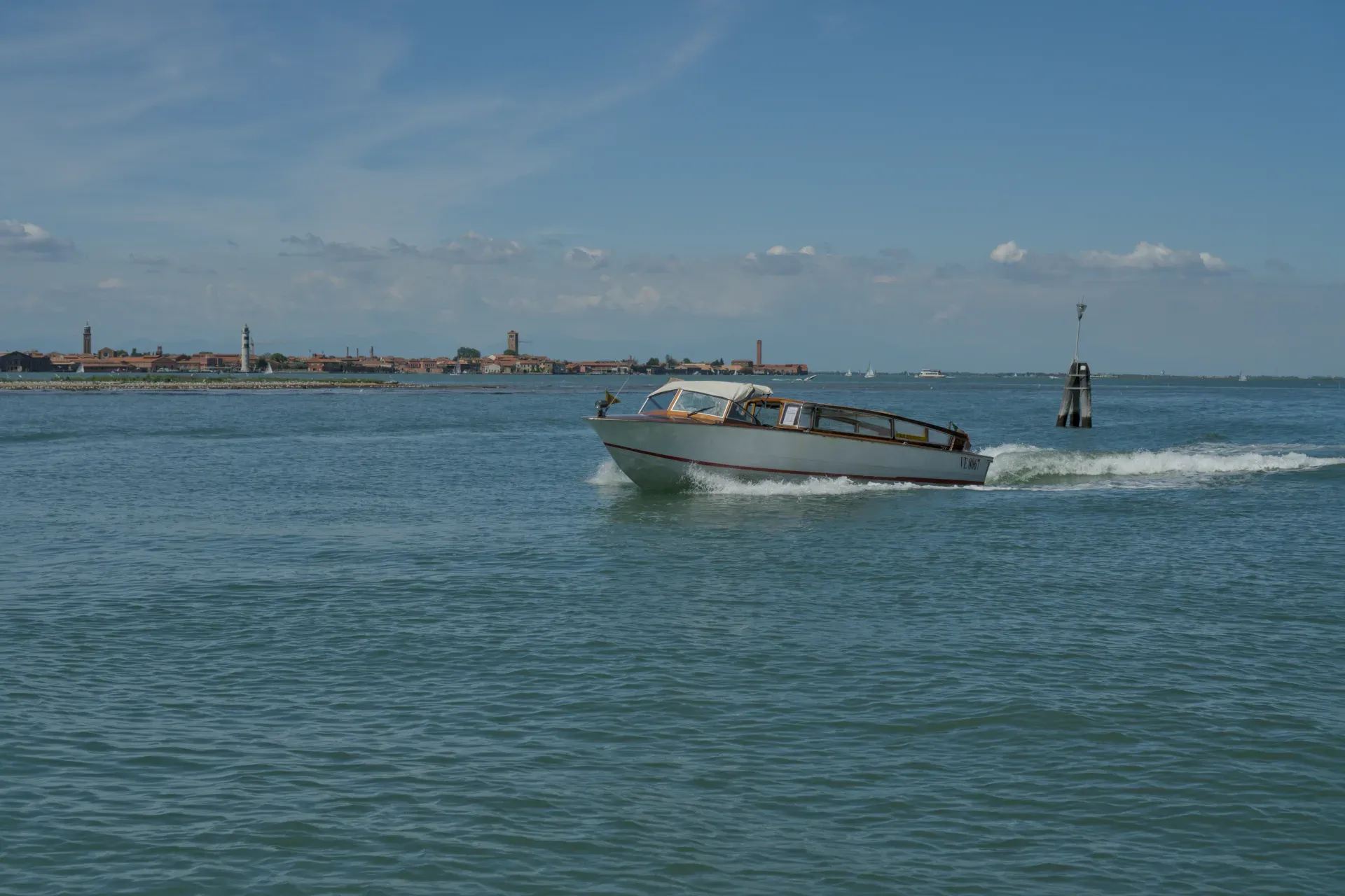 Una barca classica naviga sull'acqua blu di fronte allo skyline di Venezia in una giornata di sole.