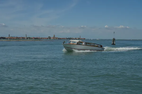Ein klassisches Boot fährt über das blaue Wasser vor der Skyline von Venedig an einem sonnigen Tag.