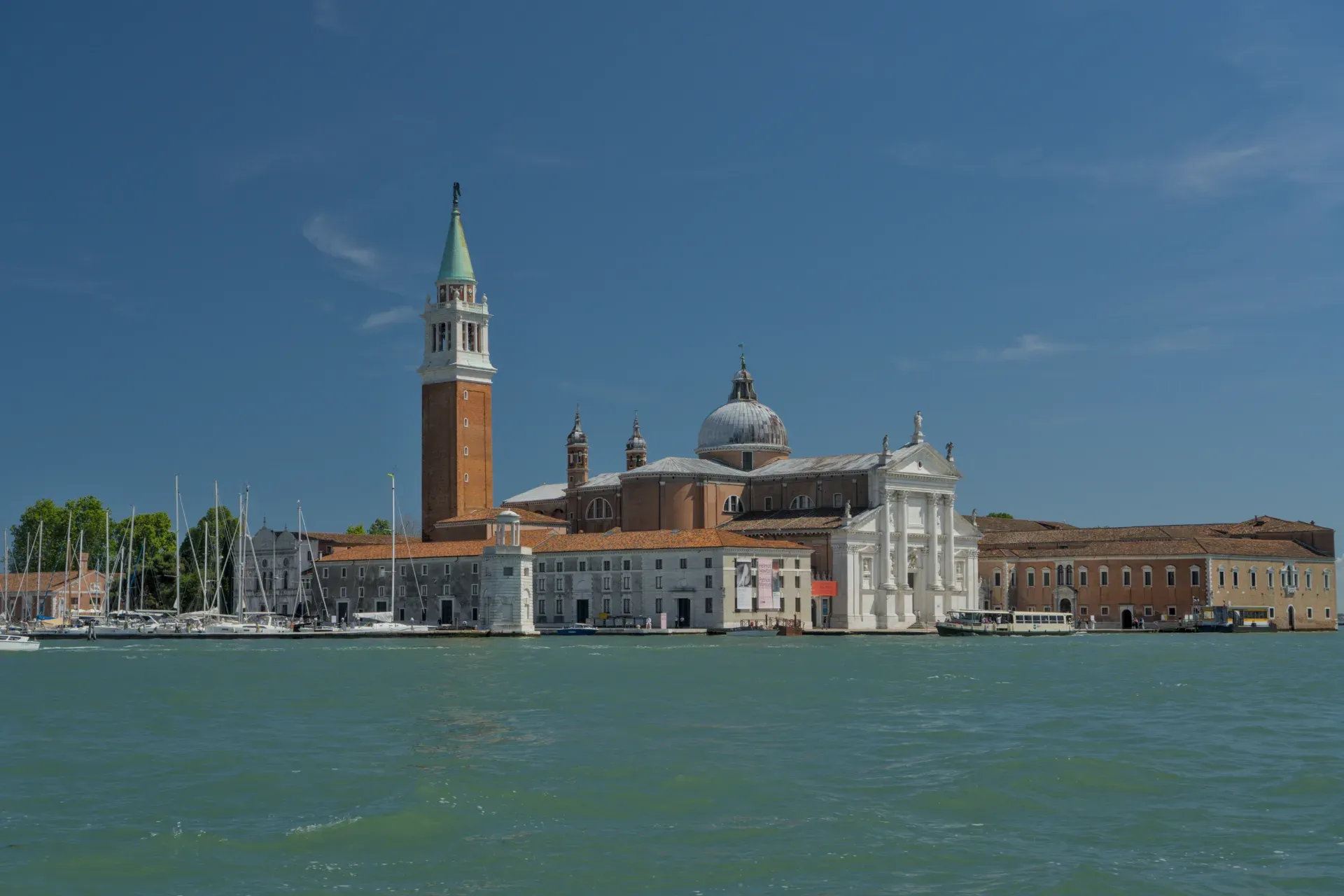 Die Basilika San Giorgio Maggiore mit ihrem Campanile in Venedig, Italien, vor einem klaren blauen Himmel und ruhigem Wasser.