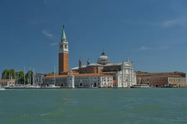 Die Basilika San Giorgio Maggiore mit ihrem Campanile in Venedig, Italien, vor einem klaren blauen Himmel und ruhigem Wasser.
