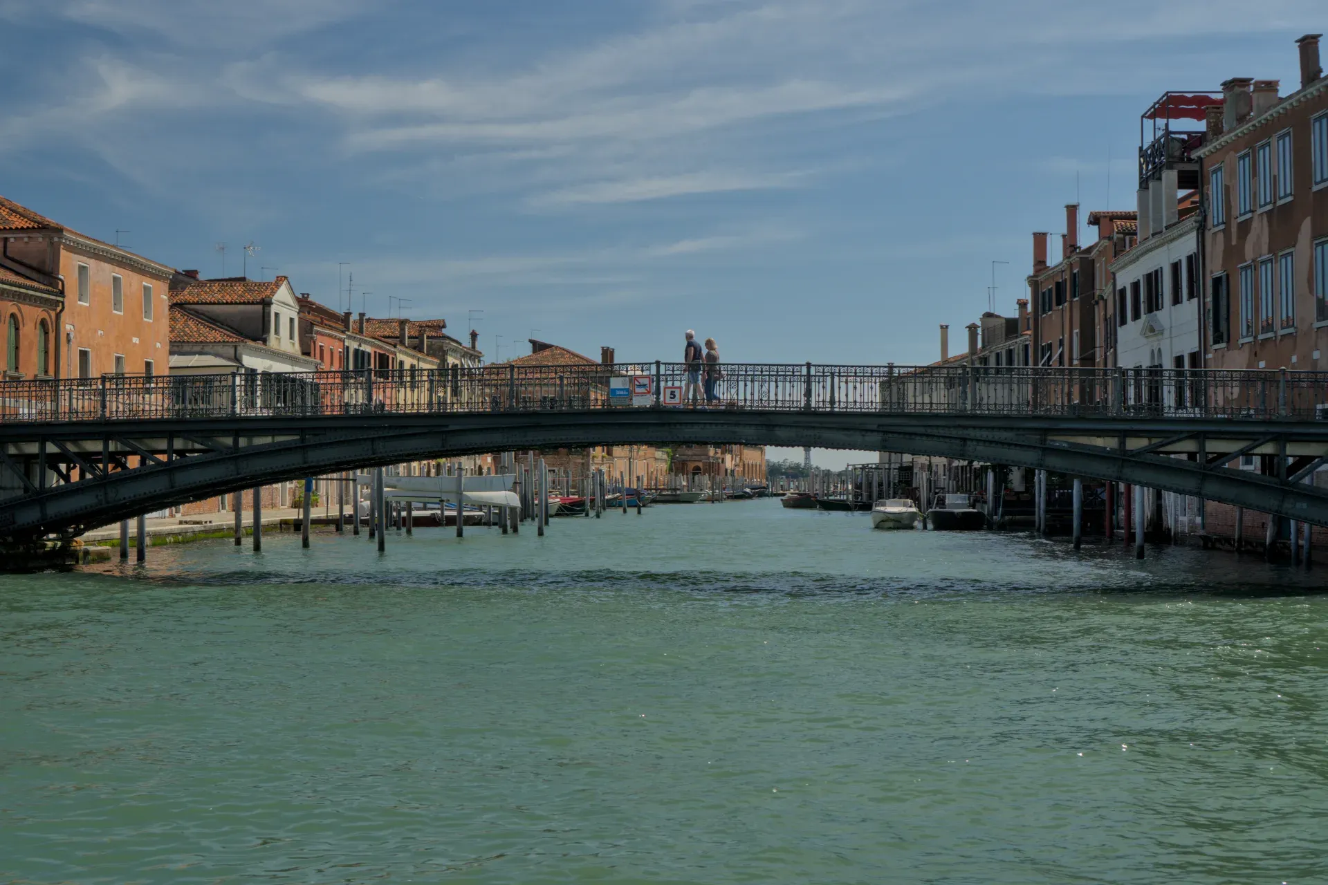 Una fotografia dettagliata di un ponte a Venezia, Italia, su un canale turchese, con edifici tradizionali e una coppia che passeggia.