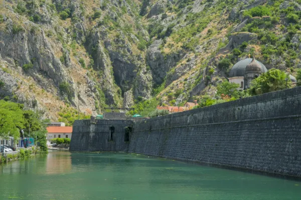 Kotor fortress wall by emerald green water, with steep mountains in the background.