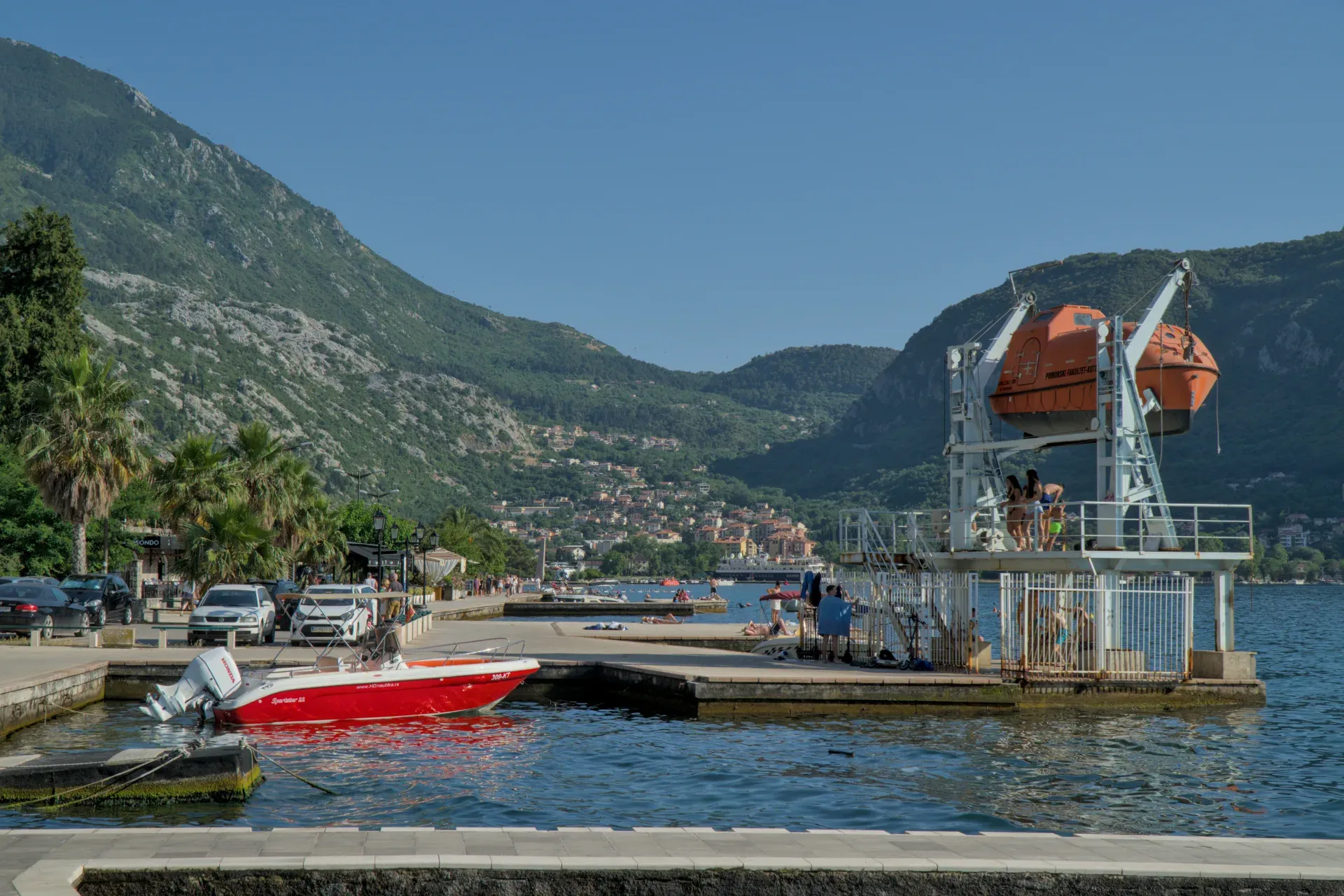 Piktoresni pogled na Kotorski zaliv u Crnoj Gori sa crvenim čamcem i čamcima za spasavanje u sunčanom danu.