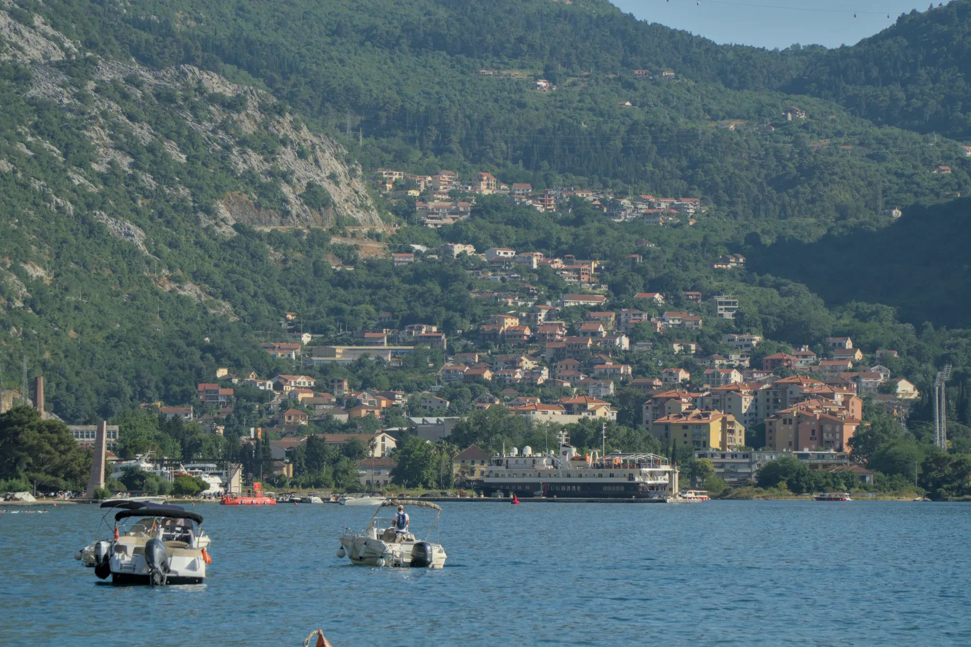 View of the Bay of Kotor with boats on the water and a city nestled against green mountain slopes.