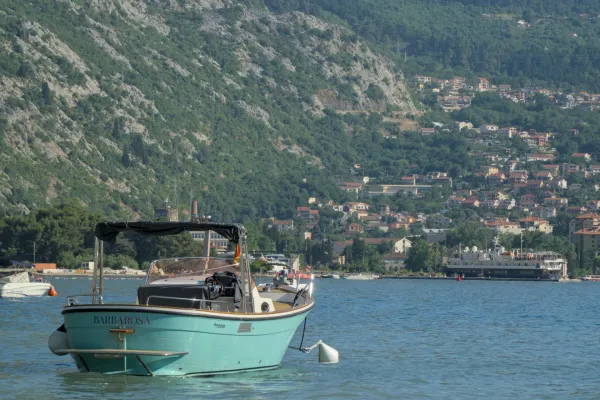 A turquoise boat rests off the coast of the Bay of Kotor, Montenegro, with green hills in the background.